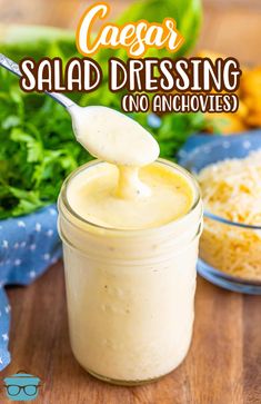 a jar filled with homemade caesar salad dressing on top of a wooden table next to vegetables