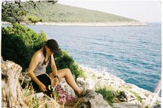 a woman sitting on top of a rock next to the ocean