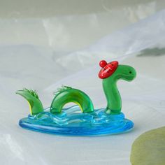 a green plastic toy with a red hat on it's head in the water