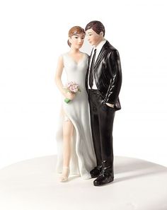 a bride and groom figurine standing next to each other on a white surface