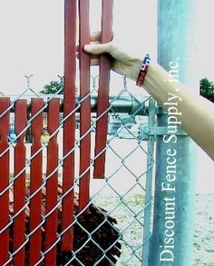 a hand is holding onto a chain link fence with dirt in the ground behind it