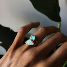 a woman's hand wearing a gold ring with two opal stones on it