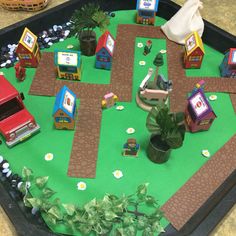 a play table with cars, houses and plants on it in the shape of a road