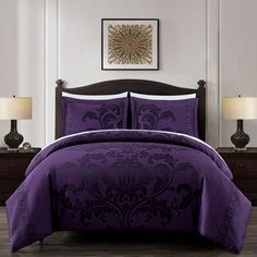 a bed with purple comforter and two lamps on the nightstands next to it