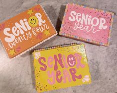 three decorated cookies with the words senior year on them are sitting on a counter top