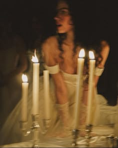 a woman sitting in front of candles with her face obscured by the candle holder behind her