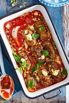 a casserole dish with meatballs and sauce on it next to a spoon