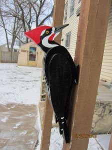 a black and white bird with a red head standing on a wooden post in the snow