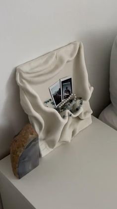 a white table topped with a vase filled with flowers and pictures next to a pillow