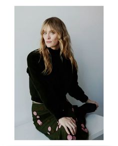 a woman sitting on top of a white table wearing a black sweater and green pants