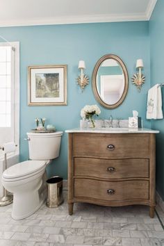 a white toilet sitting next to a bathroom sink under a mirror on top of a wooden cabinet