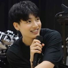 a young man holding a microphone in front of a drum set and smiling at the camera