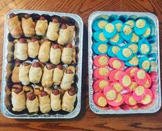 two tin trays filled with different types of pastries on top of a wooden table