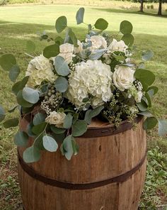 a wooden barrel with white flowers and greenery in it sitting on the ground next to grass