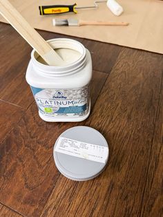 a jar of paint sitting on top of a wooden floor next to a spatula