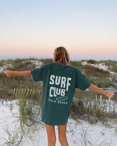 a woman standing in the sand with her arms spread out and looking at the beach