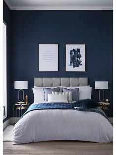 a bedroom with blue walls, white bedding and two framed pictures on the wall