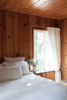 a bedroom with wood paneling and white linens on the bed, along with a window