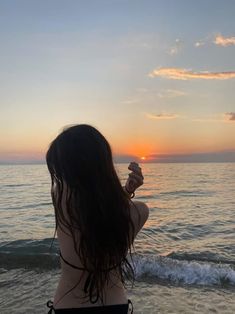 a woman standing on top of a beach next to the ocean holding a seashell