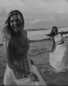 two women are running in the water at the beach, one is wearing a dress