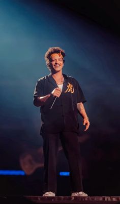 a man standing on top of a stage with a microphone in his hand and smiling at the camera