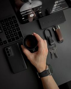 a person's hand holding a coffee cup on top of a black desk next to a laptop