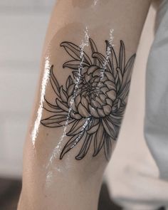 a black and white photo of a flower tattoo on the left arm with water droplets around it