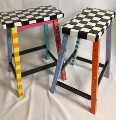 two colorful stools sitting side by side on a white sheeted surface, each with different designs and colors