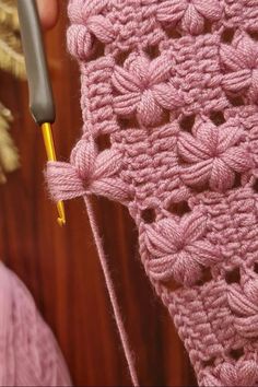 someone is crocheting the edge of a pink sweater with a yellow knitting needle