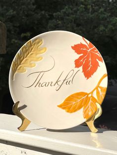 a plate with the words thank on it sitting on top of a white bench next to trees