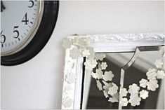 a clock is hanging on the wall next to a white frame with paper flowers and hearts