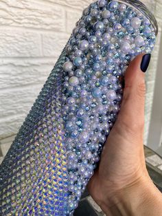 a woman's hand holding a blue and silver case with pearls on it, in front of a white brick wall