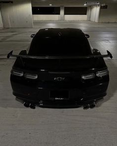 the back end of a black car in a parking garage with no one around it