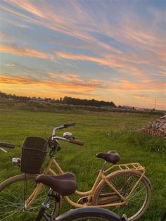 two bicycles are parked in the grass near each other on a sunny day with an orange and blue sky behind them