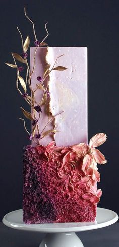 a three tiered cake with pink and purple frosting on a white pedestal in front of a dark background