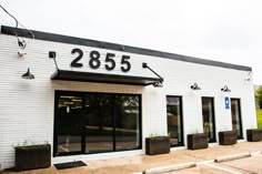 a white brick building with black numbers and planters on the front door is shown