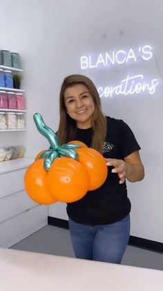 a woman holding an orange balloon in front of a white wall with the words blanca's creations on it