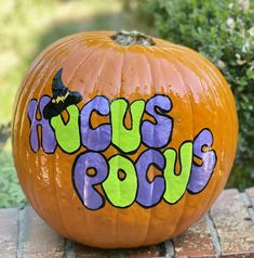 a decorated pumpkin sitting on top of a brick walkway next to bushes and trees, with the words acrylic pout painted on it