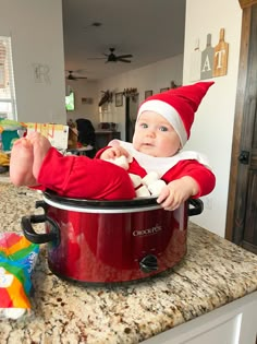 a baby wearing a santa hat sitting in a crock pot on top of a counter