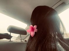 a woman's long hair with a pink flower in the back seat of a car