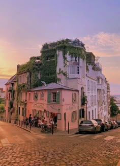 an old building with vines growing on it's roof and cars parked in the street