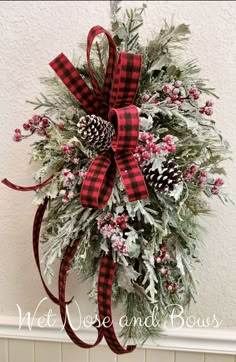 a christmas wreath with pine cones, holly and red plaid bow hanging on the wall