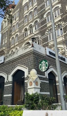 an old brick building with a starbucks sign on it's corner and bushes in front