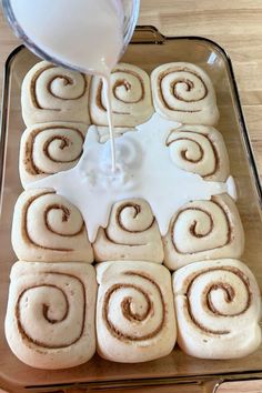 a pan filled with cinnamon rolls being drizzled with icing