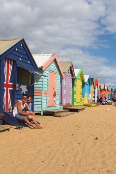 two people sitting on a bench in front of colorful beach huts with the flag of australia painted on them