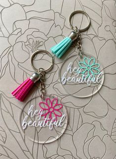 two personalized key chains with tassels on them, one has a flower and the other has a name