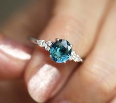 a woman's hand holding a ring with an aqua blue stone and diamond accents