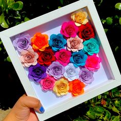 a person holding up a white box with colorful paper flowers in it's center