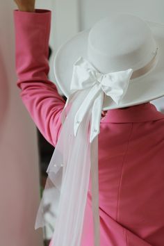 a woman in a pink dress and white hat with her hand on the back of her head