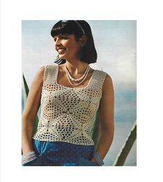 a woman wearing a crochet top and blue shorts standing in front of the ocean